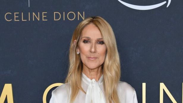 Céline Dion in weißem Outfit vor grauem Hintergrund.