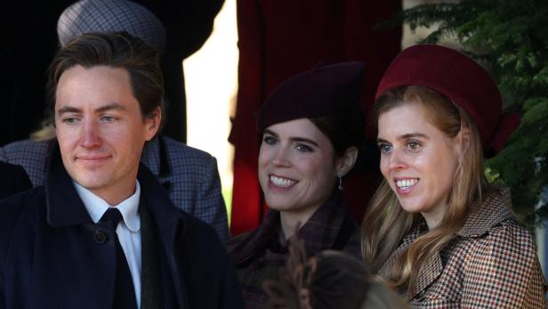 Drei lächelnde Personen, darunter Prinzessin Beatrice und Prinzessin Eugenie mit Hüten, sind zu sehen.