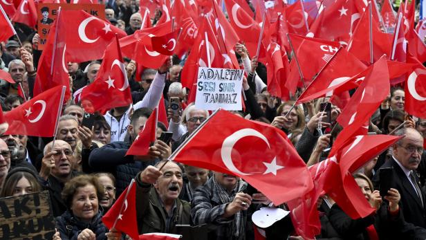 Eine Menschenmenge schwenkt türkische Flaggen und hält Schilder bei einer Kundgebung.