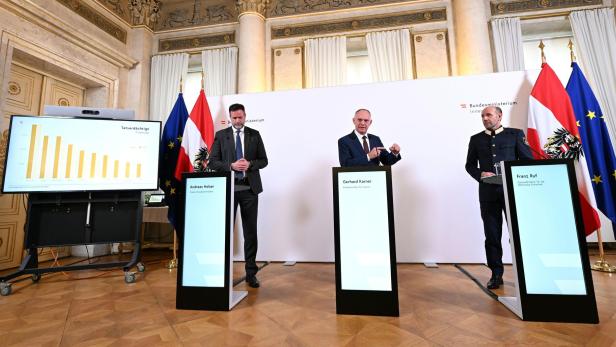 Drei Männer, darunter Gerhard Karner, stehen vor Flaggen und Bildschirmen bei einer Pressekonferenz.