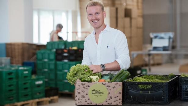 Ein blonder Mann in einem weißen Hemd mit einem Obstkorb. 