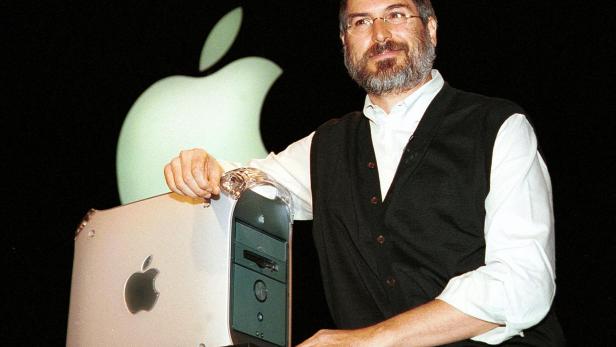 Steve Jobs präsentiert einen Apple Computer vor einem großen Apple-Logo.