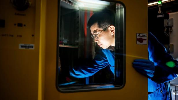 ein Mann im blauen Kittel öffnet ein Laborgerät mit verglaster Tür