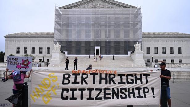 Vor einem Gerichtsgebäude halten Demonstrierende ein großes Banner mit der Aufschrift „Hands off Birthright Citizenship“.