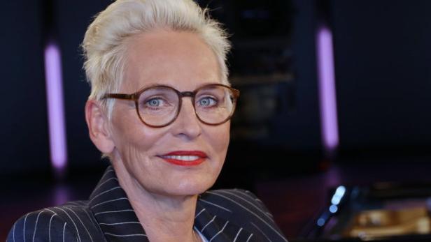 Bärbel Schäfer sitzt im gestreiften Blazer und mit rotem Lippenstift auf einem Sessel und blickt freundlich in die Kamera.