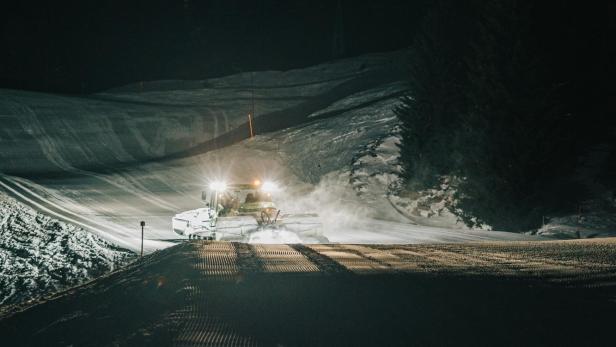 Beleuchtete Pistenraupe im Schnee bei Nacht