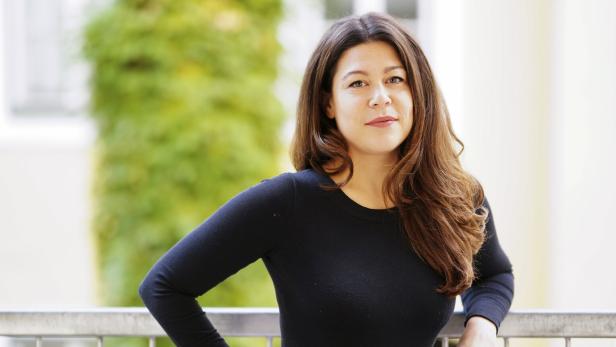 Eine Frau mit braunen, gewellten Haaren lehnt an einem Geländer.