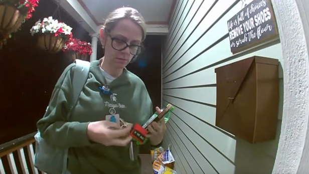 Eine erschöpfte Frau steht mit Ausweis und Schlüsseln vor einer Haustür im Eingangsbereich.