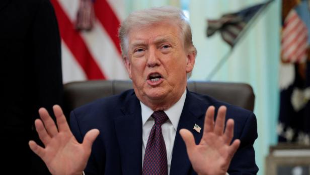 Donald Trump gestikuliert vor US-Flaggen mit erhobenen Händen.