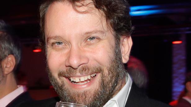 Christian Ulmen lächelt mit Glas in der Hand.