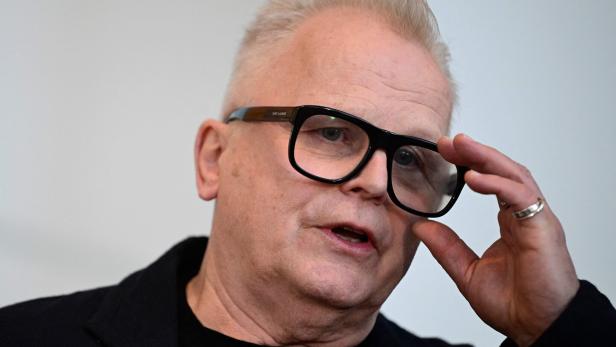 Herbert Grönemeyer mit hellen Haaren und schwarzer Jacke hält seine schwarze Brille fest.
