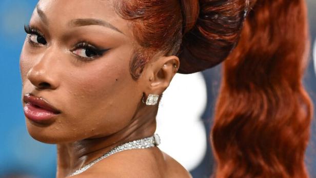 Megan Thee Stallion mit hochgesteckten, kupferroten Haaren, verziert mit Strasssteinen, blickt über ihre Schulter.