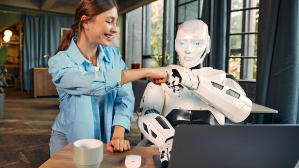 Frau und humanoider Roboter geben sich im Büro einen freundschaftlichen Faustgruß.