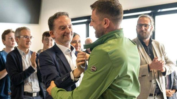 Zwei Männer begrüßen sich herzlich, während andere applaudieren.