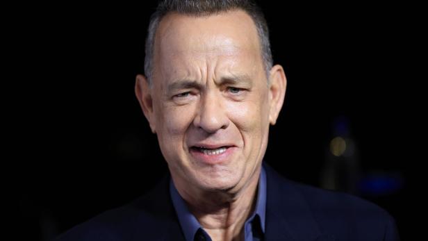 Tom Hanks lächelt vor einem dunklen Hintergrund.