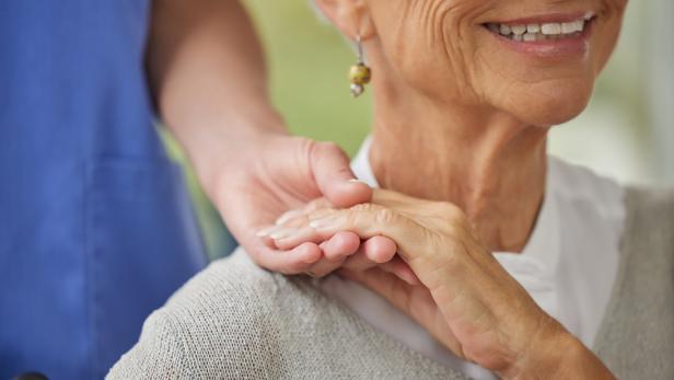 Eine ältere Frau lächelt, während eine andere Person fürsorglich ihre Hand hält.