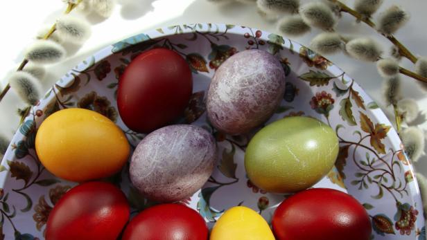 Bunte Ostereier auf einem dekorativen Teller mit Weidenkätzchen im Hintergrund.