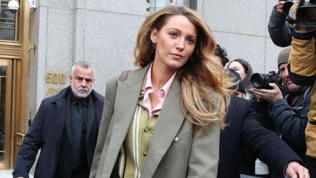 Blake Lively in einem übergroßen Anzug geht an Kameras und einem Gebäude vorbei.