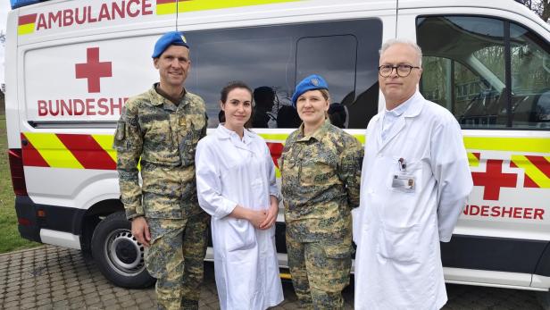 Zwei Personen in Militäruniform und zwei in weißer Kleidung stehen vor einem Rettungswagen mit der Aufschrift „Bundesheer“.