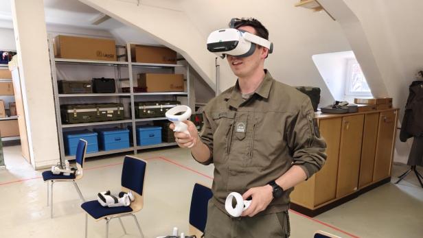 Eine Person in Uniform nutzt eine Virtual-Reality-Brille mit Controllern in einem Raum mit Stühlen und Regalen.