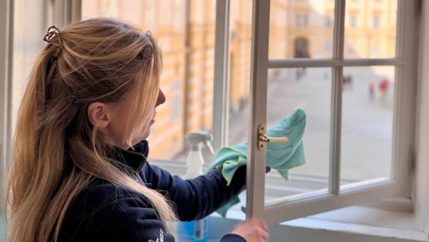 Frau reinigt ein geöffnetes Fenster im Stift Melk mit Blick auf den barocken Innenhof.