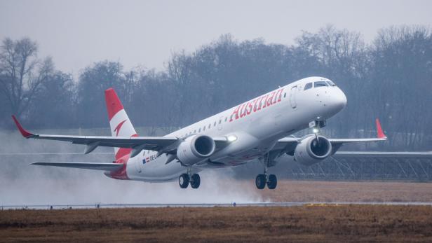Eine Austrian Airlines Maschine startet auf einer nassen Landebahn.