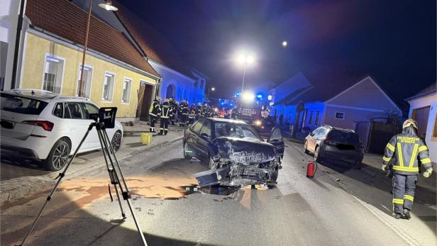 Ein Unfallauto mit stark beschädigter Front steht auf einer nächtlichen Straße, umgeben von Feuerwehrleuten und Einsatzfahrzeugen.