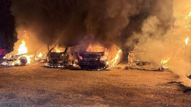 Mehrere Autos stehen in Flammen, dichter Rauch steigt in die Nacht auf, im Vordergrund ein Schotterplatz.