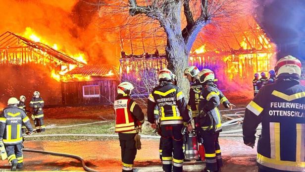 Mehrere Feuerwehrleute bekämpfen einen Großbrand in einem brennenden Gebäude bei Nacht.