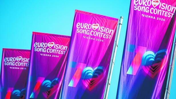 Mehrere bunte Fahnen mit der Aufschrift „Eurovision Song Contest Vienna 2026“ wehen vor blauem Himmel.