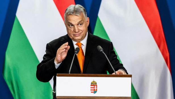Viktor Orbán spricht vor ungarischen Flaggen an einem Rednerpult mit Wappen.