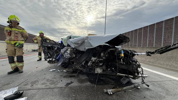 Zwei Feuerwehrleute stehen neben einem stark zerstörten Autowrack auf einer Autobahn.