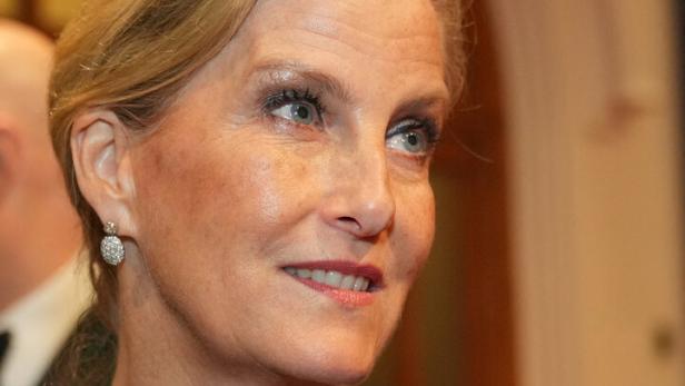 Herzogin Sophie mit Halskette und Brosche in Marineblau blickt lächelnd zur Seite.