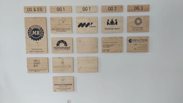 Holzschilder mit verschiedenen Firmenlogos und Beschriftungen an einer weißen Wand montiert.