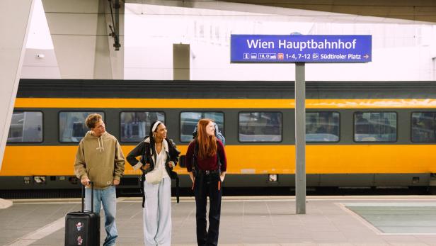 Drei junge Menschen mit Gepäck am Bahnsteig des Wiener Hauptbahnhofs vor einem Zug.