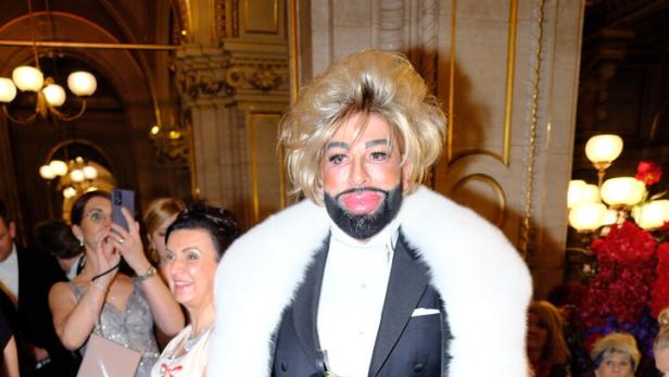 Harald Glööckler im Smoking mit Pelzmantel auf dem roten Teppich.