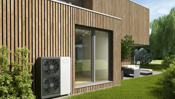 Ein modernes Haus mit Holzfassade, Wärmepumpe und großem Fenster zum Garten.