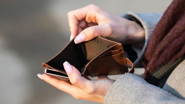 Leere Geldbörse wird von einer Person mit lackierten Fingernägeln in den Händen gehalten.