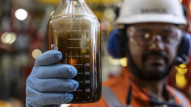 Ölbohr-Arbeiter hält Flasche mit Rohöl in die Kamera.