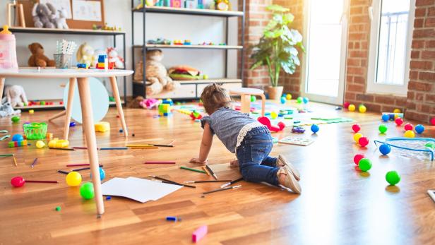 Beautiful toddler crawling on the floor around lots of toys at kindergarten