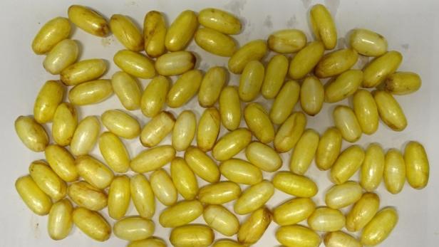 Viele gelbe, längliche Kapseln liegen auf einer hellen Oberfläche.