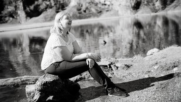 Eins chwarz-weißes-Bild einer Frau, die an einem Wasser auf einem Baumstamm sitzt