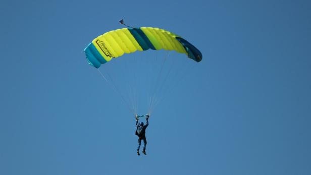 Fallschirmspringer mit geöffnetem gelb-blauem Schirm vor wolkenlosem Himmel.