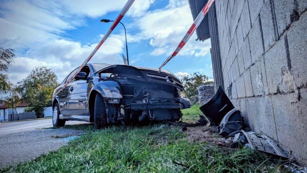 Ein Auto mit beschädigter Front steht neben einer Mauer, Trümmerteile liegen auf dem Boden, Absperrband ist gespannt.