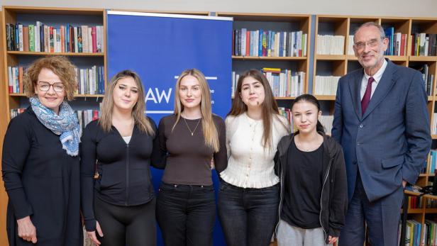 Sechs Personen stehen lächelnd vor Bücherregalen und einem blauen Aufsteller nebeneinander.