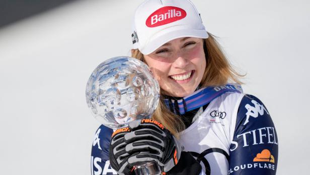 Eine lächelnde Mikaela Shiffrin mit Barilla-Kappe hält eine Kristallkugel-Trophäe.