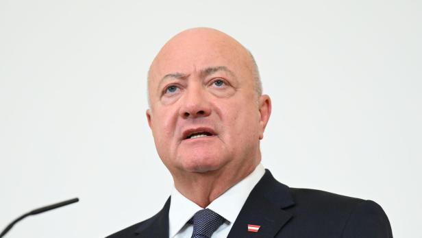 Ein Mann im Anzug mit Österreich-Anstecker spricht vor einem Mikrofon.