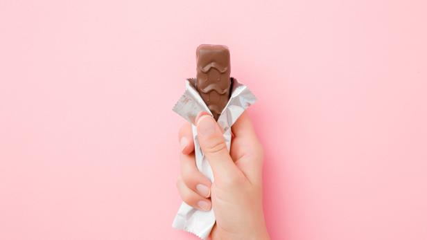 Young woman hand holding chocolate bar on pastel pink table. Opened pack. Sweet snack. Closeup. Top view.