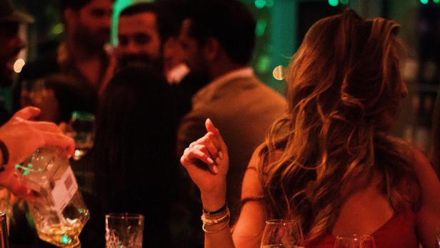 Menschen unterhalten sich und trinken an einer Bar bei gedämpftem Licht.