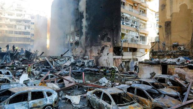 Ausgebrannte Autos, Trümmer und rauchende, stark beschädigte Gebäude mit Feuerwehrleuten und Rettungskräften.
